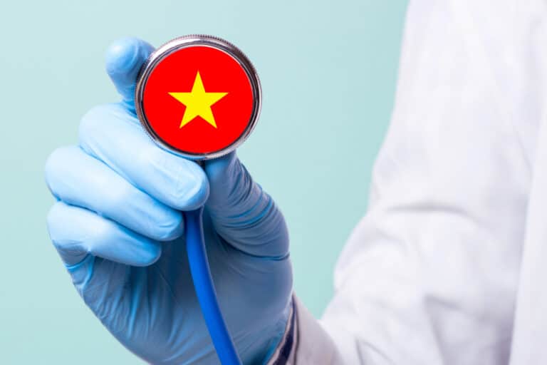 A gloved hand holding a stethoscope with a Vietnamese flag